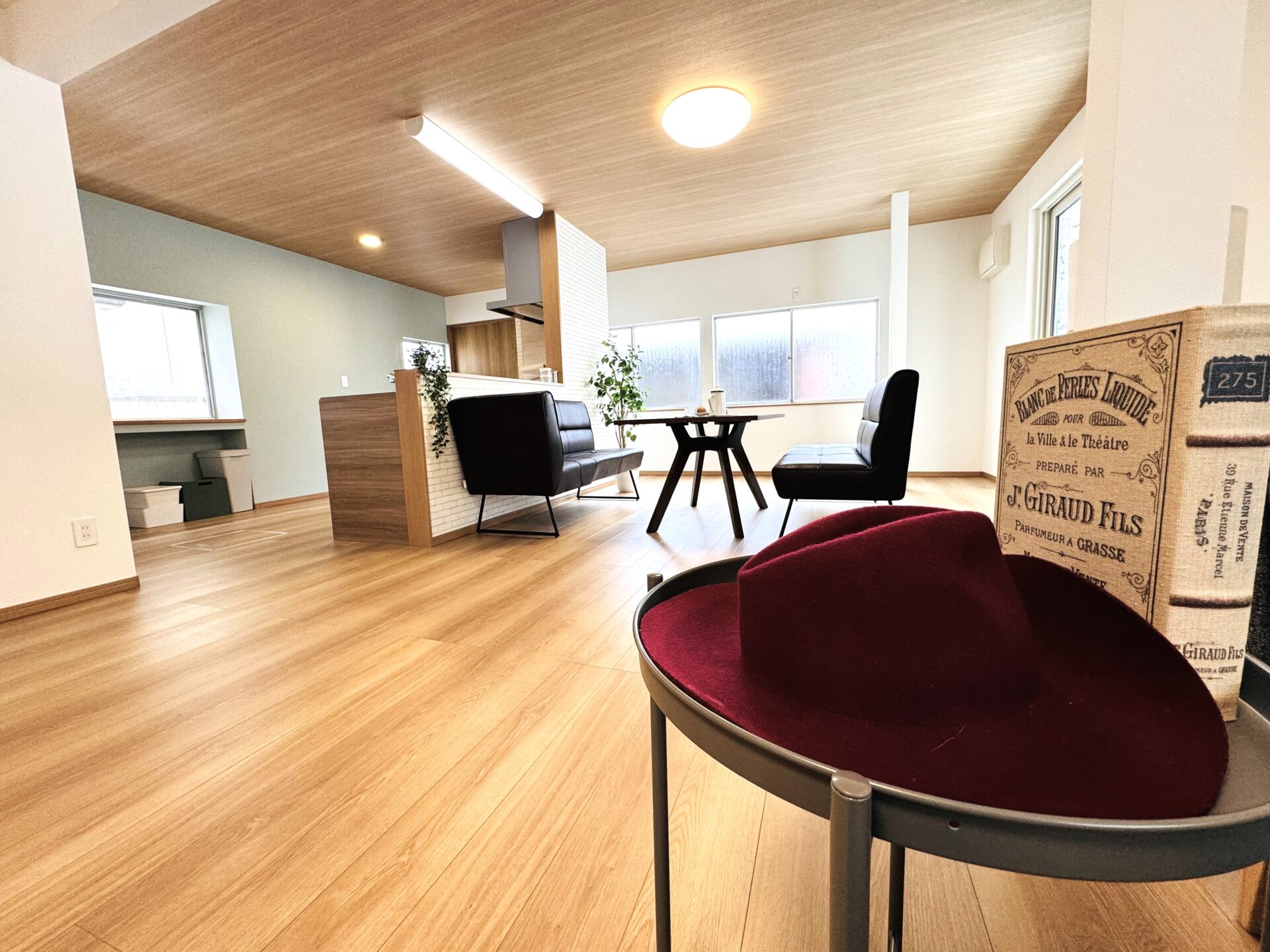 シンプルでスタイリッシュな日本のリビングルーム。キッチン島、ダイニングテーブル、そしてサイドテーブルに置かれたフェドーラハットとリキュールの本。